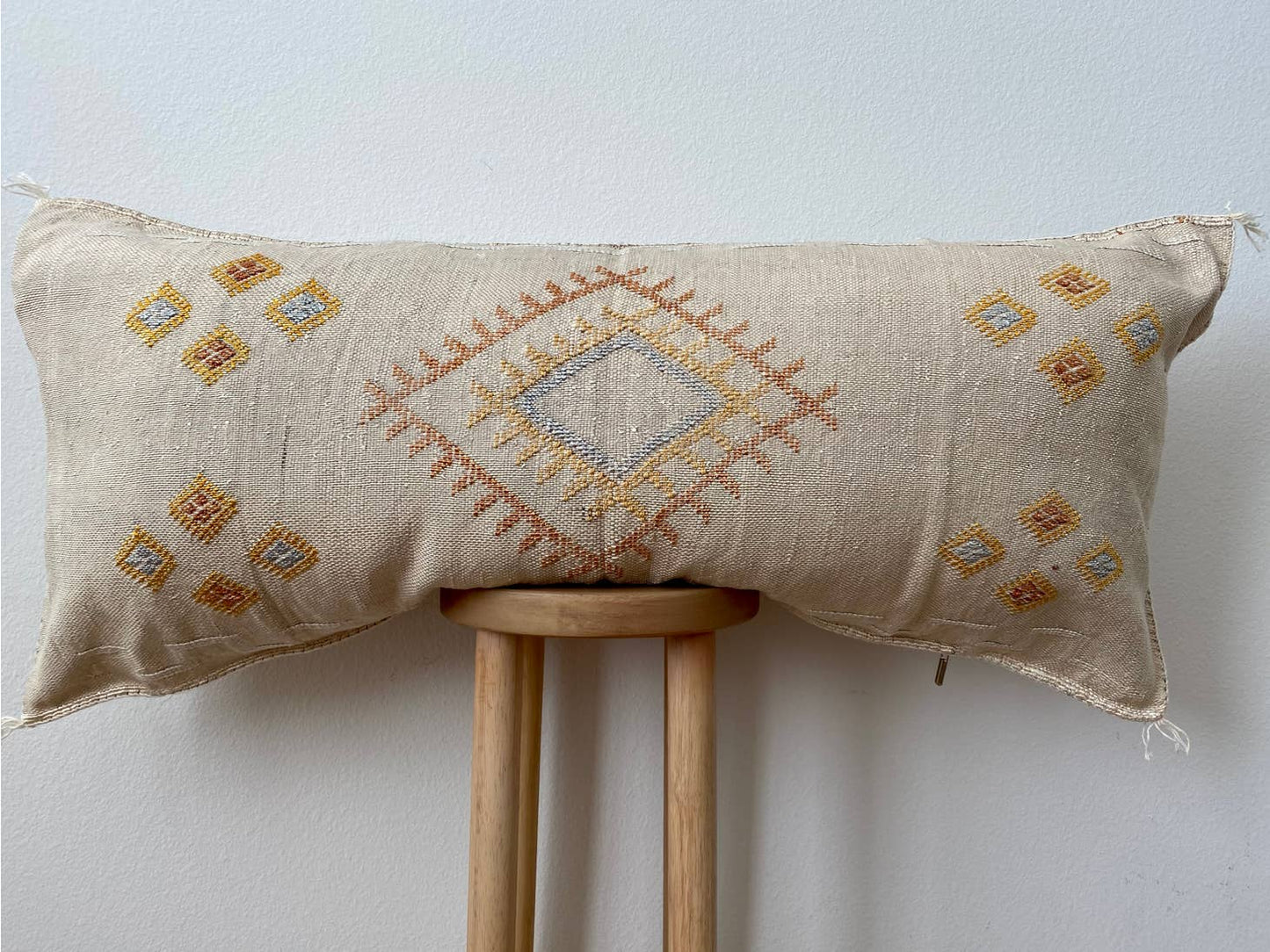 One-of-a-kind Sabra bolster pillow made with a natural silk fiber from the agave cactus plant. Features hand-stitched embroidery. Each of these pillows is one-of-a-kind, meaning that the pillow shipped will be grey but the color and designs will vary. Includes a down pillow insert.