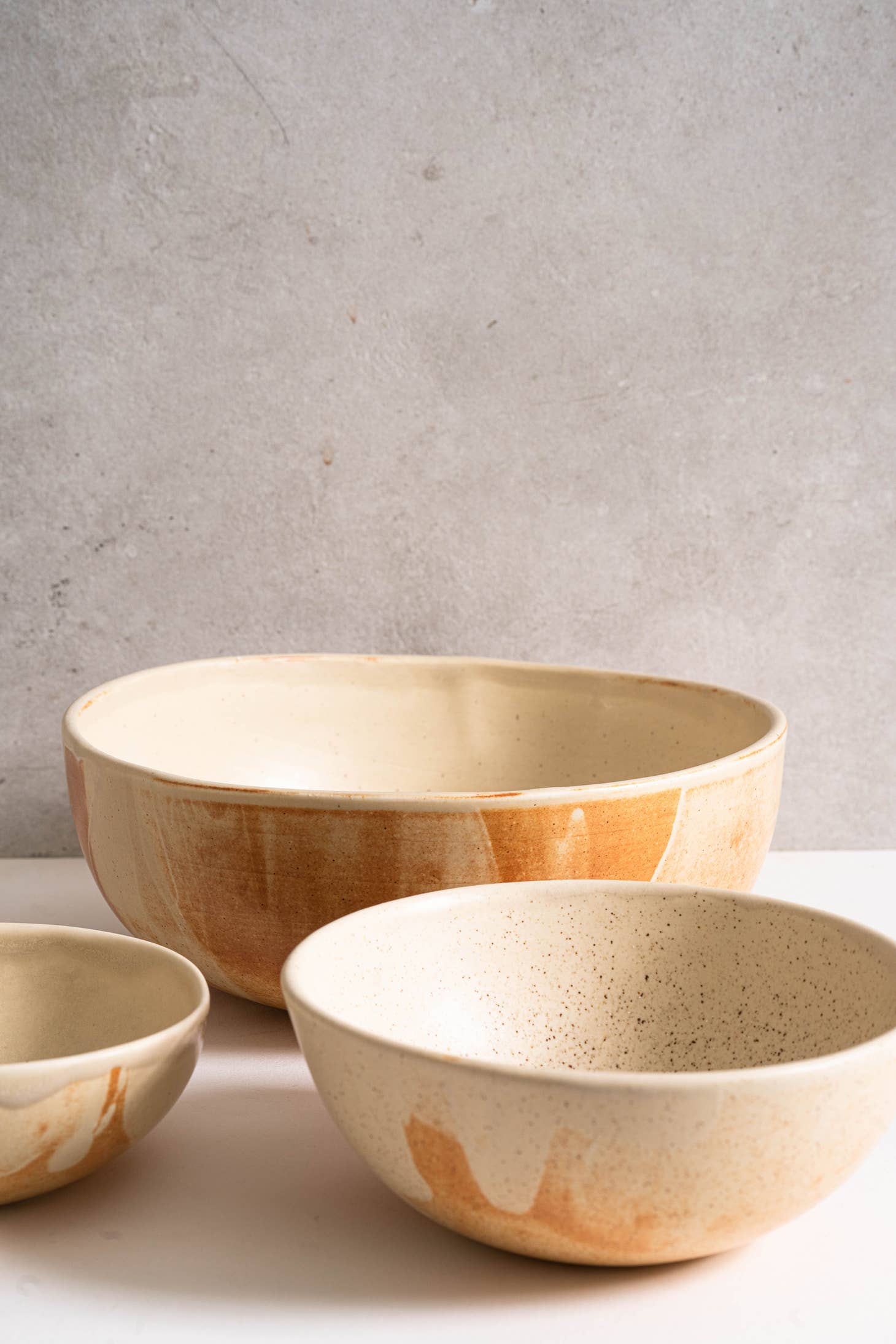 Set of 3 ceramic nesting bowls with a caramel beige matte finish. Hand-dipped in a reactive glaze that swirls uniquely across each piece and leaves beautiful rust color strokes. Handmade in Ukraine.