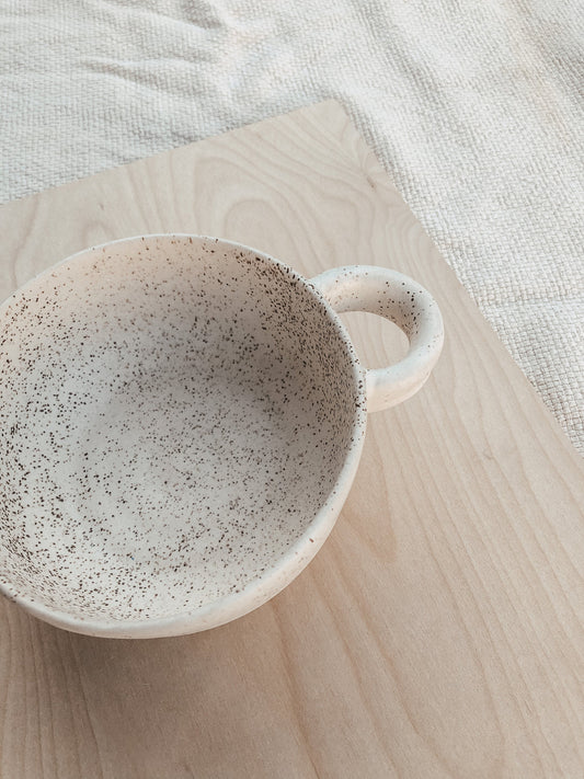 Made with a white clay and a creamy white and speckled glaze. Complete with a little half circle handle. Enjoying your food in something beautiful is always a sweet way to connect with the food that nourishes your vessel.