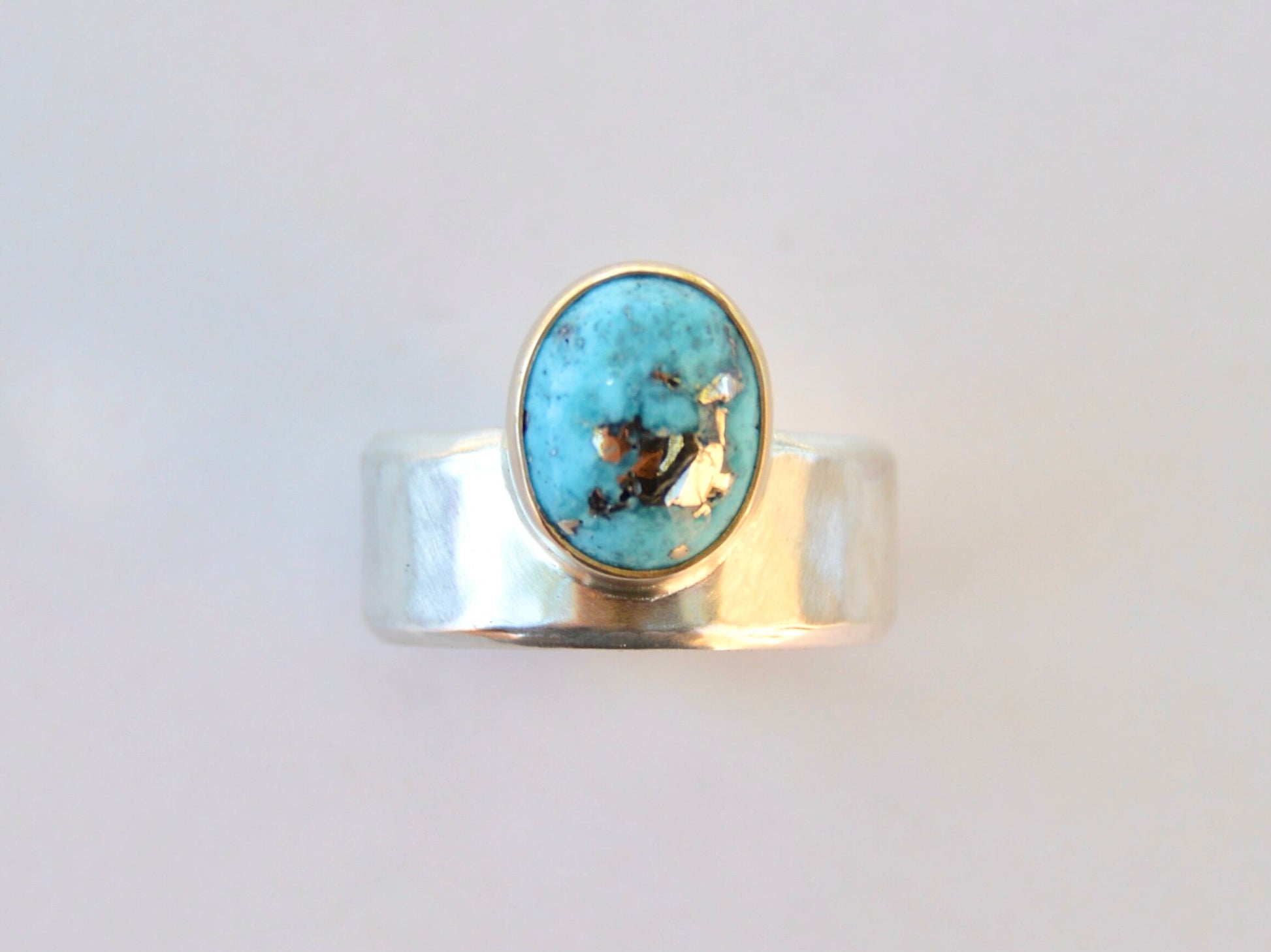 Made by hand in Northern New Mexico using recycled metals and responsibly sourced stones. This ring features a large cabochon Persian Turquoise stone set in a 14k yellow Gold bezel on a wide Sterling Silver band with matte finish.    Mesa Ring by Halcyon Jewelry.
