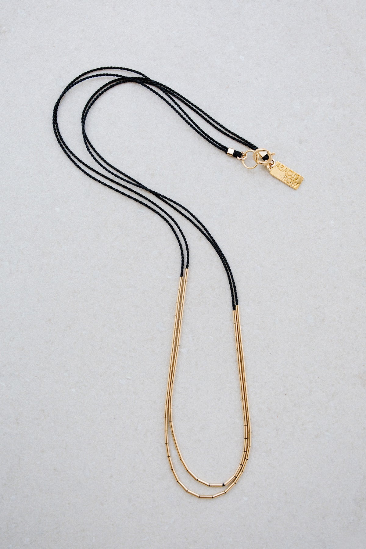 The Andromeda Necklace handmade in San Fransisco, California by Abacus Row features 14k gold tubes strung on two black silk cords