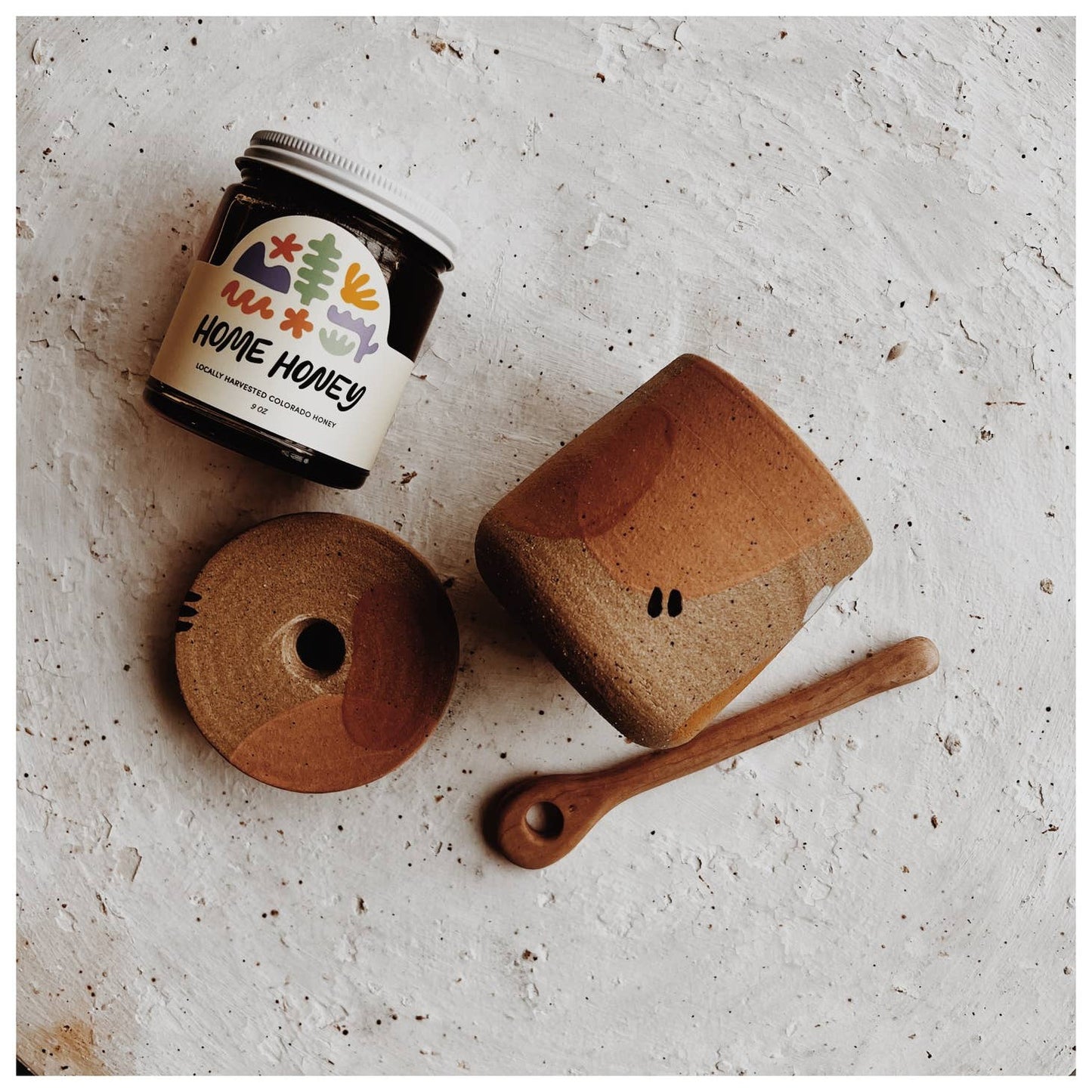 Painted dune honey pot with hand carved stick.  Glazed interior with raw clay exterior. Painted accents in dusty pink, burnt orange and light blue with black specks. Each piece is crafted by the same set of hands, which belong to Andi at Good Hearted Woman. Based in Denver, CO.