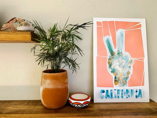 Print of an original watercolor by local Encinitas, California artist, Tait Hawes. Measures 11" x 17" features peace fingers with the word "California" underneath in peach and blue tones.