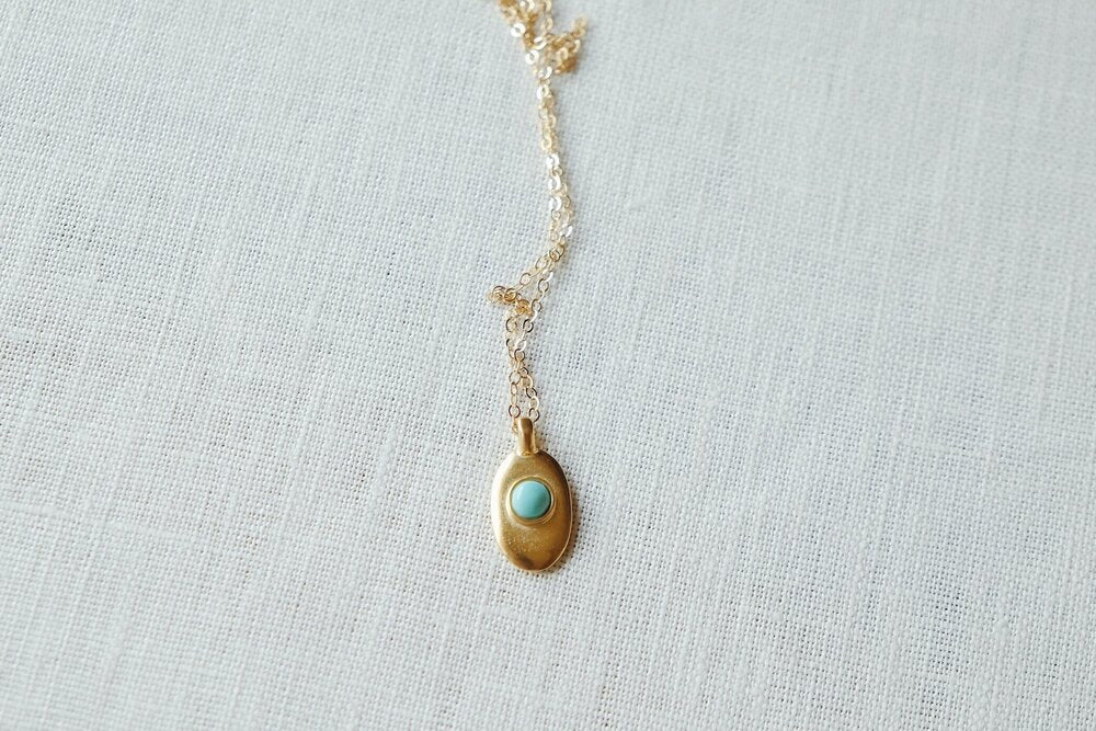 Sweet little handmade charm necklace featuring an ethically-mined turquoise stone. Available in bronze with gold plating and a gold filled chain or sterling silver chain.